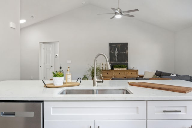 kitchen featuring vaulted ceiling, light stone counters, white cabinetry, and sink