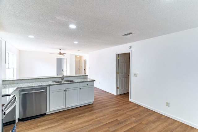 kitchen featuring light wood-type flooring, light stone counters, stainless steel appliances, sink, and a textured ceiling