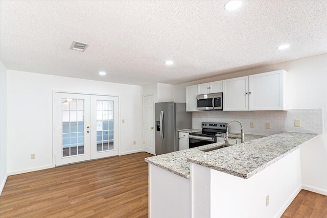 kitchen with light hardwood / wood-style flooring, stainless steel appliances, kitchen peninsula, and white cabinetry