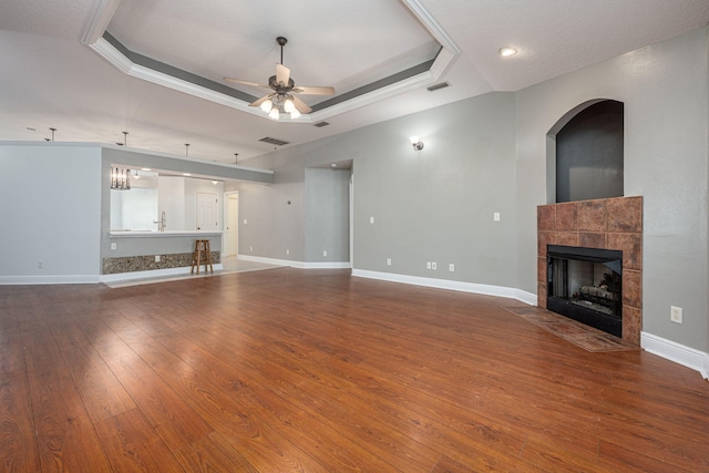 unfurnished living room with a tiled fireplace, a tray ceiling, hardwood / wood-style floors, and ceiling fan