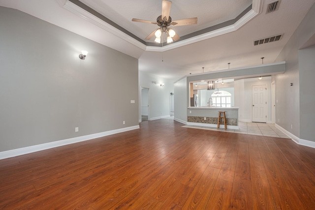 unfurnished living room featuring ceiling fan with notable chandelier, light wood-type flooring, a raised ceiling, and sink