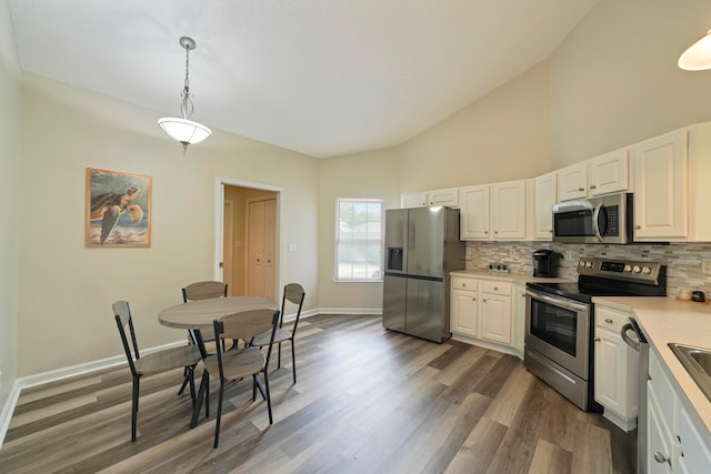 kitchen featuring decorative light fixtures, backsplash, white cabinetry, stainless steel appliances, and dark hardwood / wood-style flooring