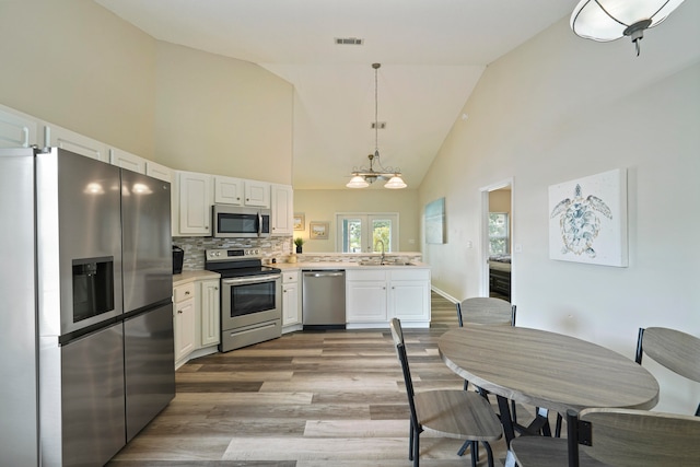 kitchen featuring wood-type flooring, stainless steel appliances, high vaulted ceiling, and white cabinetry