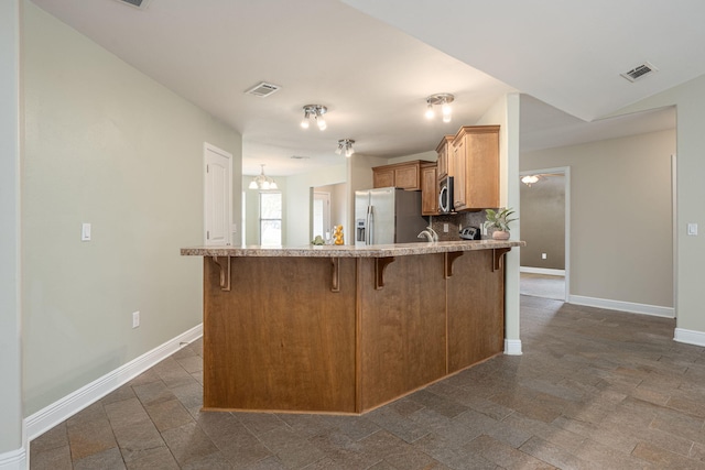 kitchen with decorative backsplash, kitchen peninsula, a breakfast bar area, and appliances with stainless steel finishes