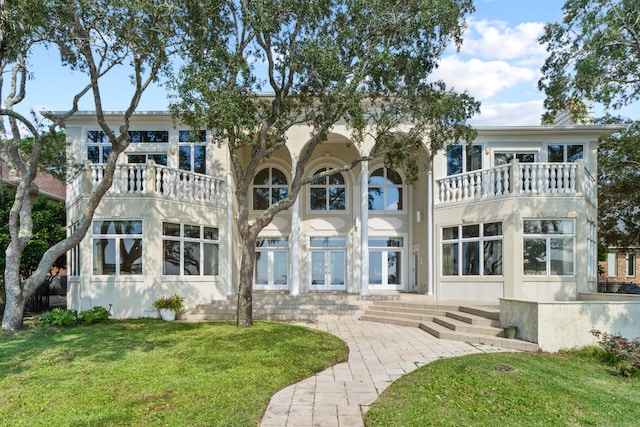 rear view of house with french doors, a lawn, a balcony, and stucco siding