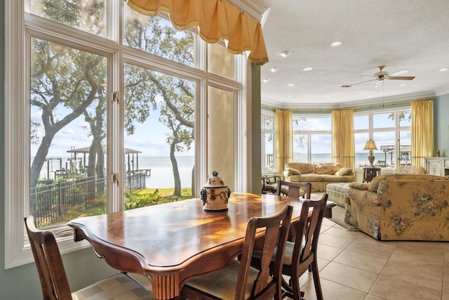 dining area with light tile patterned floors, a textured ceiling, a water view, a ceiling fan, and crown molding