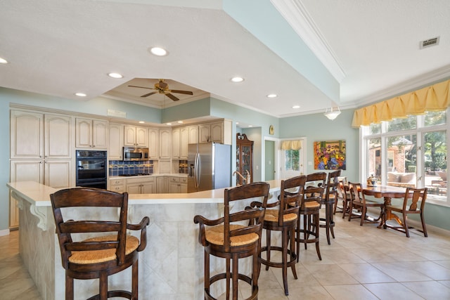 kitchen with crown molding, visible vents, cream cabinets, appliances with stainless steel finishes, and a kitchen breakfast bar