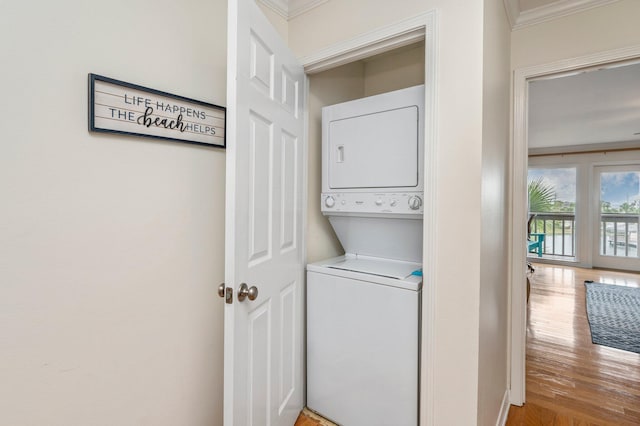 clothes washing area featuring ornamental molding, stacked washer and dryer, and hardwood / wood-style flooring