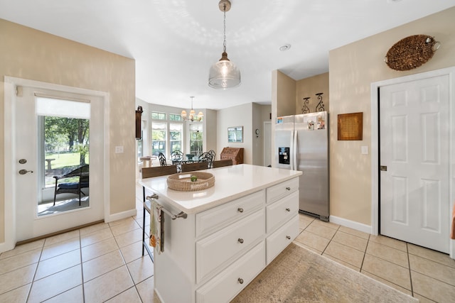 kitchen with stainless steel fridge, a kitchen island, decorative light fixtures, white cabinets, and light tile patterned floors