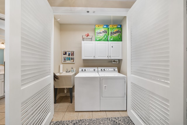 clothes washing area featuring washing machine and dryer, sink, light tile patterned floors, and cabinets