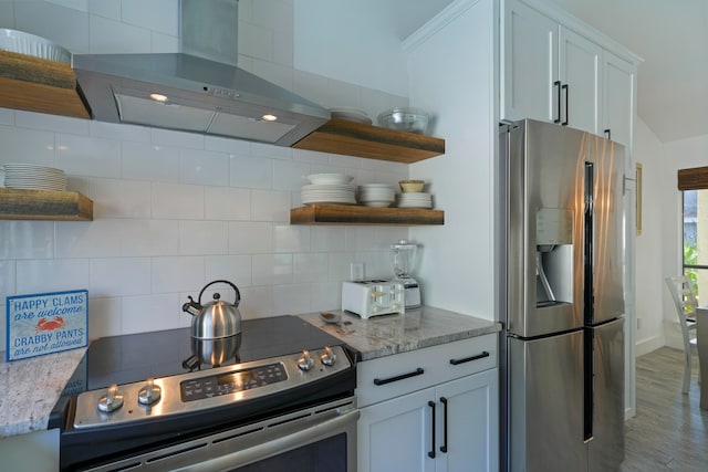 kitchen featuring white cabinets, stainless steel appliances, wall chimney range hood, and decorative backsplash