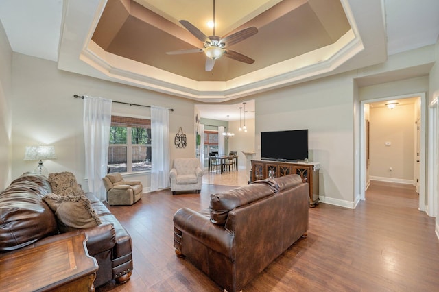 living room with ceiling fan with notable chandelier, hardwood / wood-style flooring, and a raised ceiling