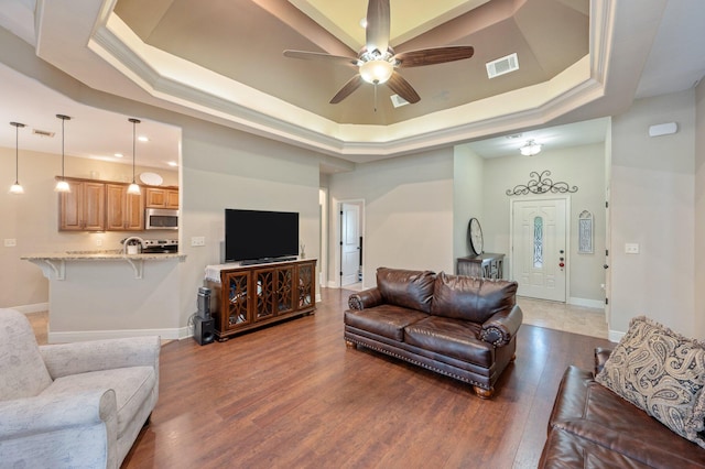 living room featuring a tray ceiling, ceiling fan, and dark wood-type flooring