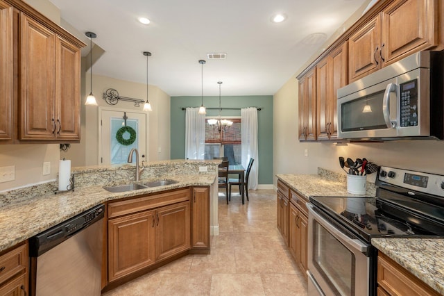 kitchen with pendant lighting, sink, an inviting chandelier, appliances with stainless steel finishes, and light stone countertops