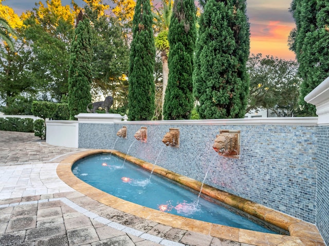 pool at dusk featuring a patio area, pool water feature, and a hot tub