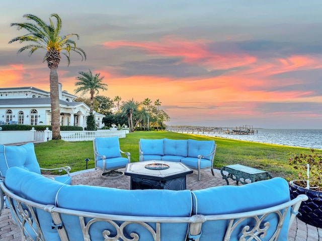 patio terrace at dusk featuring a yard, a water view, and an outdoor fire pit