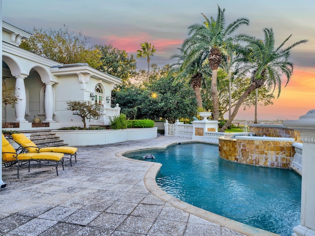 pool at dusk with an in ground hot tub and a patio