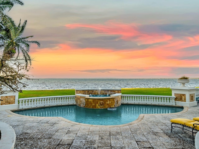 pool at dusk with an in ground hot tub, a water view, and pool water feature