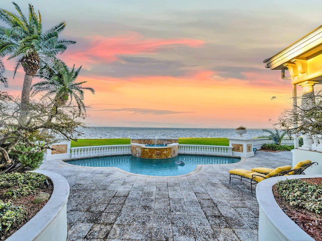 pool at dusk featuring a patio area, an in ground hot tub, and a water view