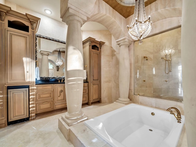 bathroom with a notable chandelier, vanity, tiled tub, and decorative columns