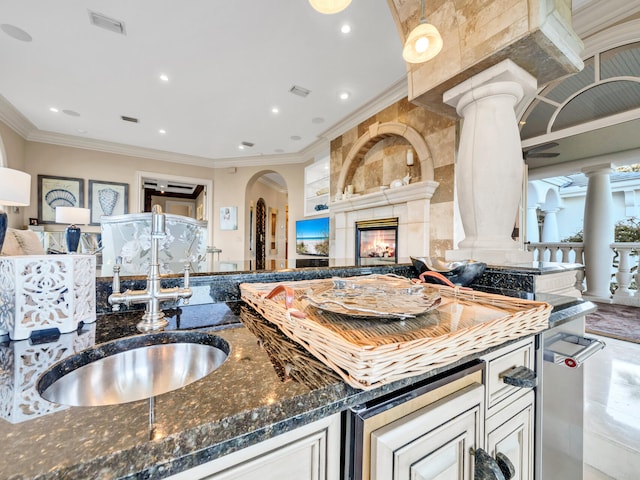 kitchen with dark stone countertops, a large fireplace, ornamental molding, and sink