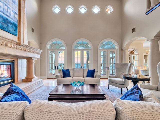 living room featuring ornate columns, a premium fireplace, french doors, and a high ceiling