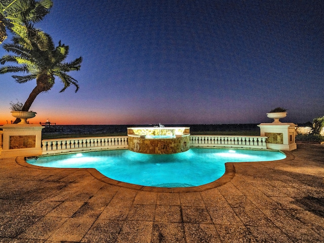 pool at dusk featuring a patio area, an in ground hot tub, a water view, and exterior fireplace