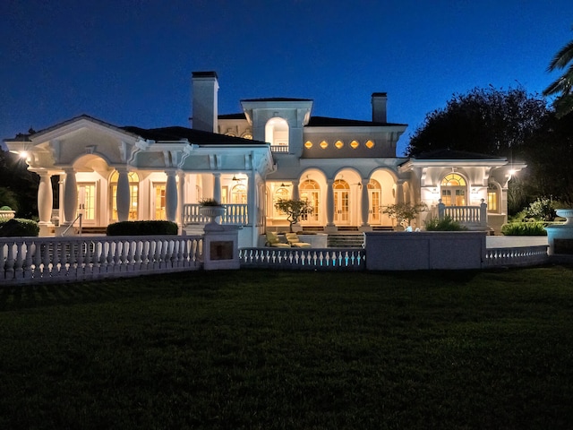 back house at night featuring a lawn and covered porch