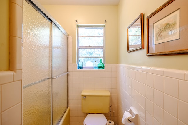 bathroom with tile walls, shower / bath combination with glass door, and toilet