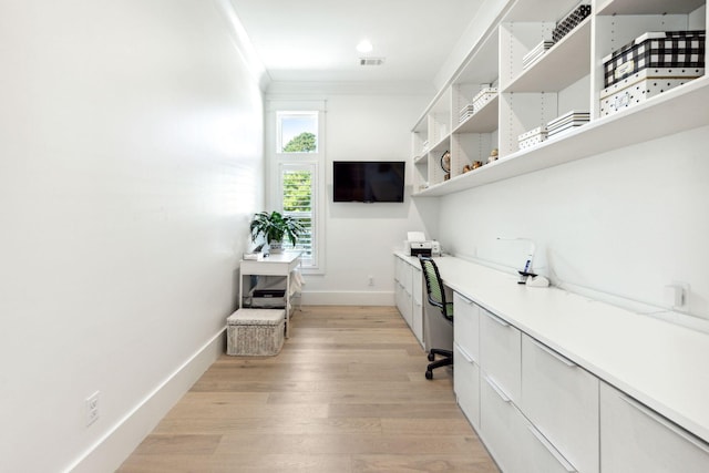 office area with built in desk, crown molding, and light wood-type flooring