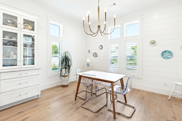 dining area featuring crown molding, a notable chandelier, light wood-type flooring, and wooden walls