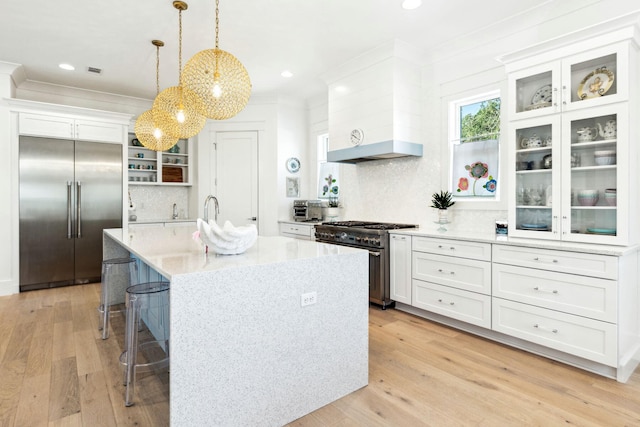 kitchen featuring hanging light fixtures, high end appliances, a center island with sink, light wood-type flooring, and white cabinetry