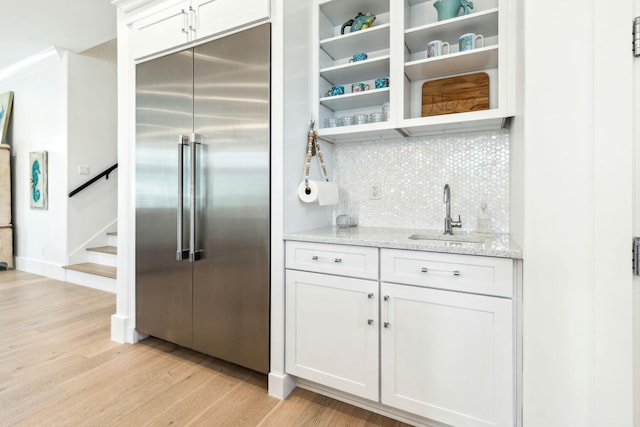 kitchen with decorative backsplash, built in fridge, sink, white cabinetry, and light hardwood / wood-style floors