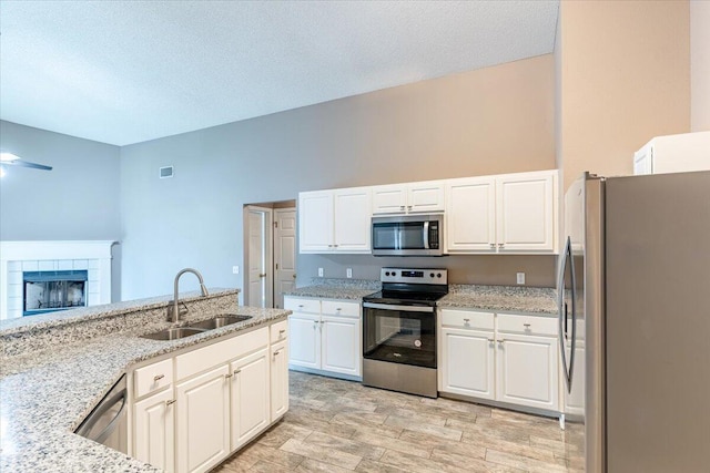 kitchen featuring light stone counters, sink, a tiled fireplace, white cabinetry, and stainless steel appliances