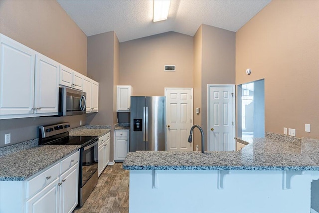 kitchen featuring kitchen peninsula, white cabinetry, appliances with stainless steel finishes, a breakfast bar area, and dark hardwood / wood-style flooring