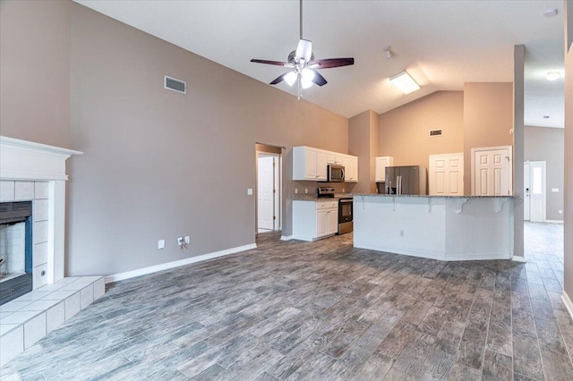 kitchen featuring hardwood / wood-style floors, stainless steel appliances, white cabinets, a tiled fireplace, and a kitchen bar