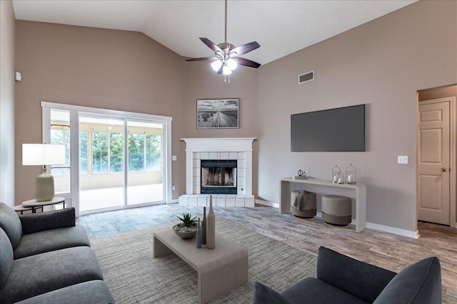 living room featuring ceiling fan, light wood-type flooring, high vaulted ceiling, and a tiled fireplace