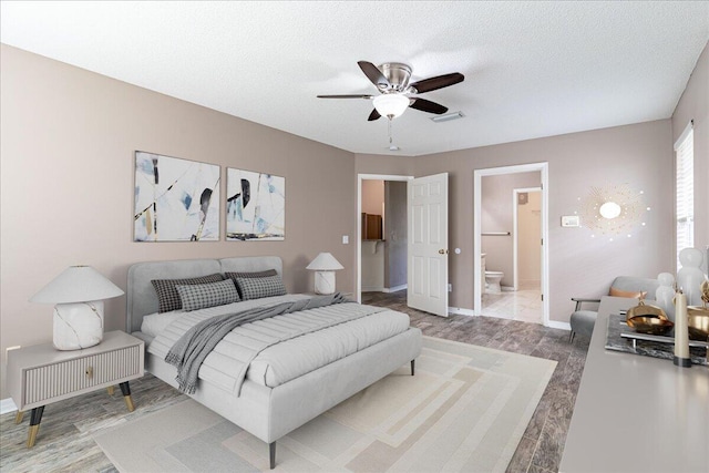 bedroom featuring ensuite bath, ceiling fan, wood-type flooring, and a textured ceiling