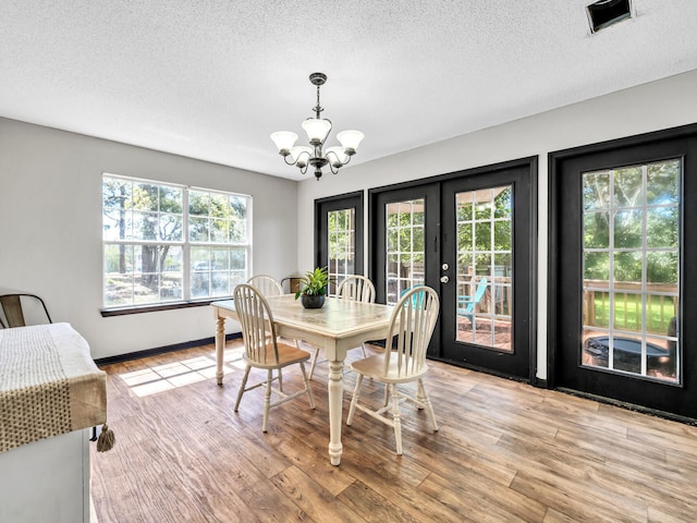 dining area featuring french doors, light hardwood / wood-style floors, a chandelier, and a textured ceiling