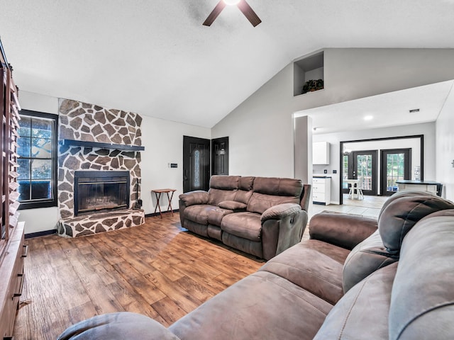 living room featuring light wood-type flooring, a fireplace, ceiling fan, and high vaulted ceiling