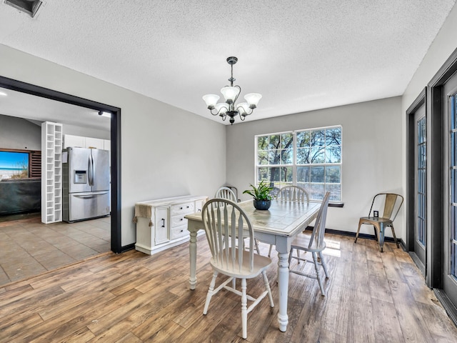 dining room featuring a textured ceiling, a notable chandelier, and light hardwood / wood-style flooring