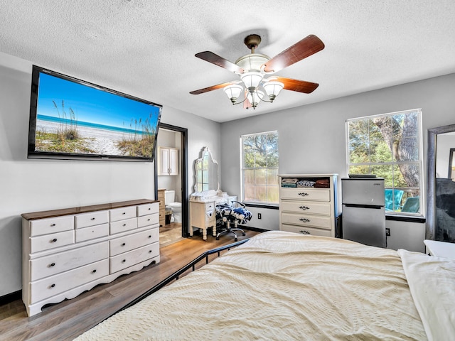 bedroom featuring stainless steel fridge, ceiling fan, wood-type flooring, and a textured ceiling