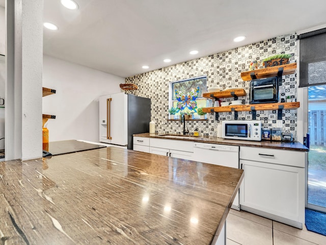 kitchen featuring high quality fridge, stovetop, sink, decorative backsplash, and white cabinetry