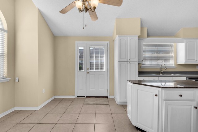 kitchen featuring sink, dark stone countertops, light tile patterned floors, ceiling fan, and white cabinets