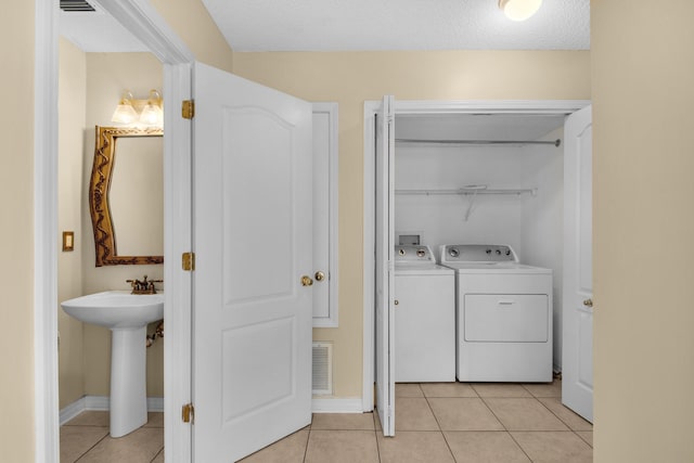 washroom featuring separate washer and dryer, sink, light tile patterned floors, and a textured ceiling