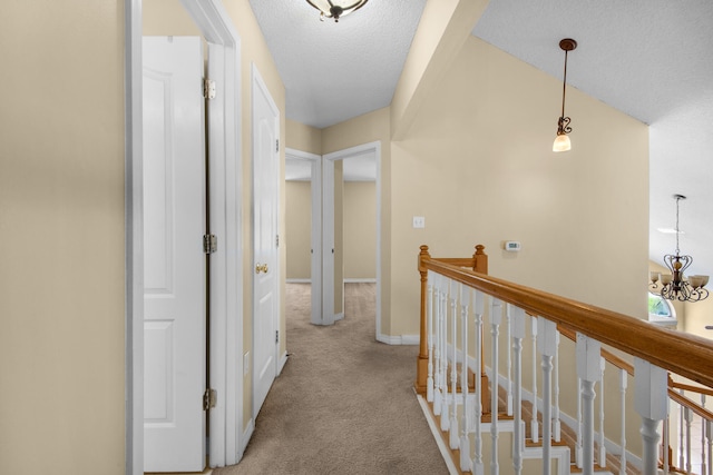 hall featuring light colored carpet, a chandelier, and a textured ceiling