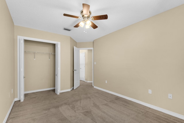 unfurnished bedroom featuring light carpet, a textured ceiling, a closet, and ceiling fan