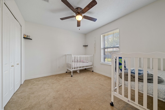 carpeted bedroom featuring ceiling fan, a nursery area, a textured ceiling, and a closet