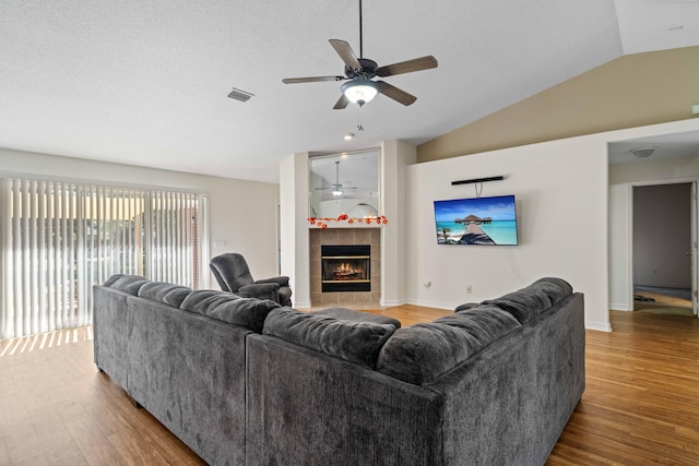 living room featuring ceiling fan, a tile fireplace, vaulted ceiling, and wood-type flooring