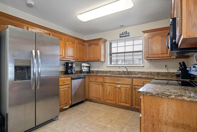 kitchen with dark stone countertops, appliances with stainless steel finishes, sink, and a textured ceiling